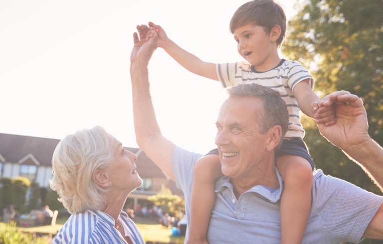 A happy older couple lifts a child into the air, representing love and family connection in a warm setting.